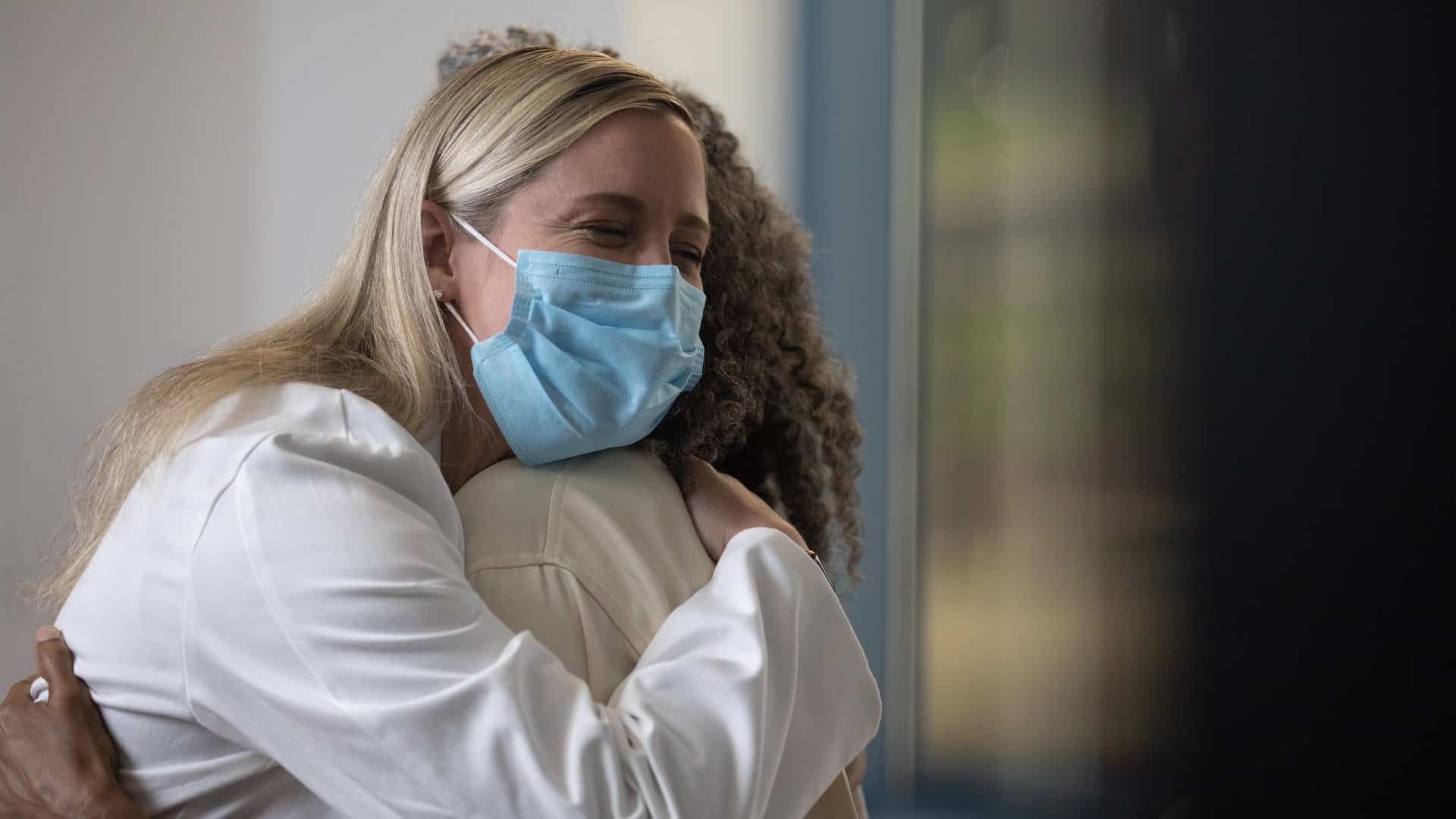 Physician in white coat and mask hug a patient.