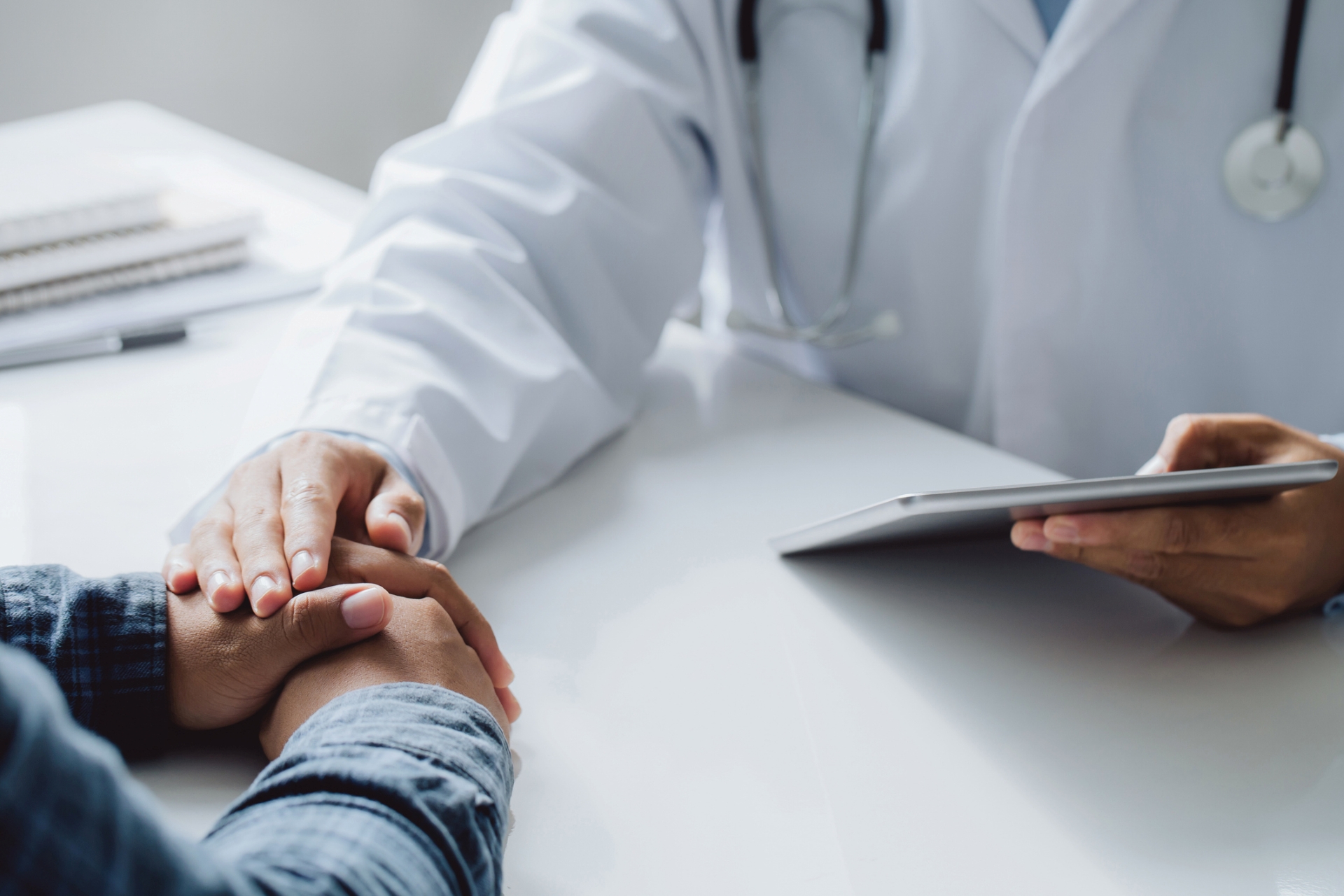 Physician comforts a patient by touching their hand. 