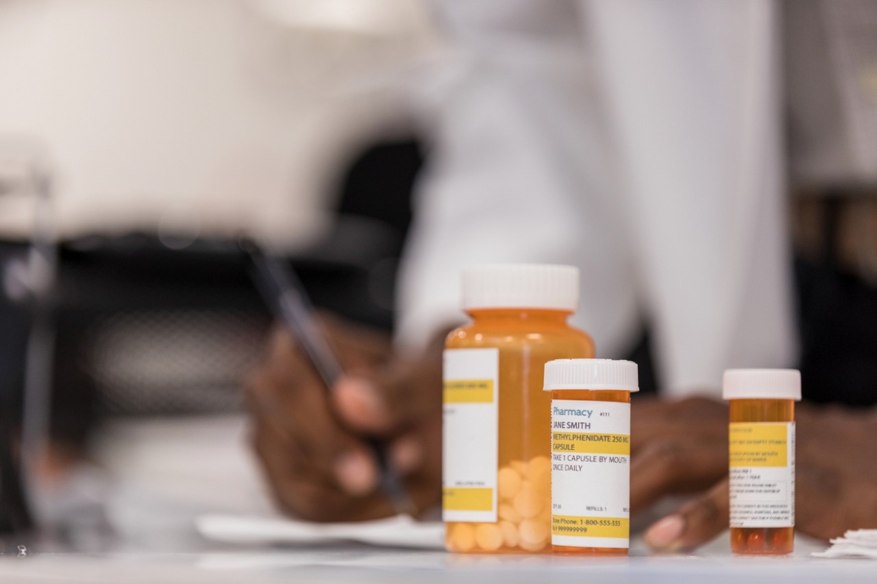 Physician writes on a notepad with a prescription bottle in the foreground. 