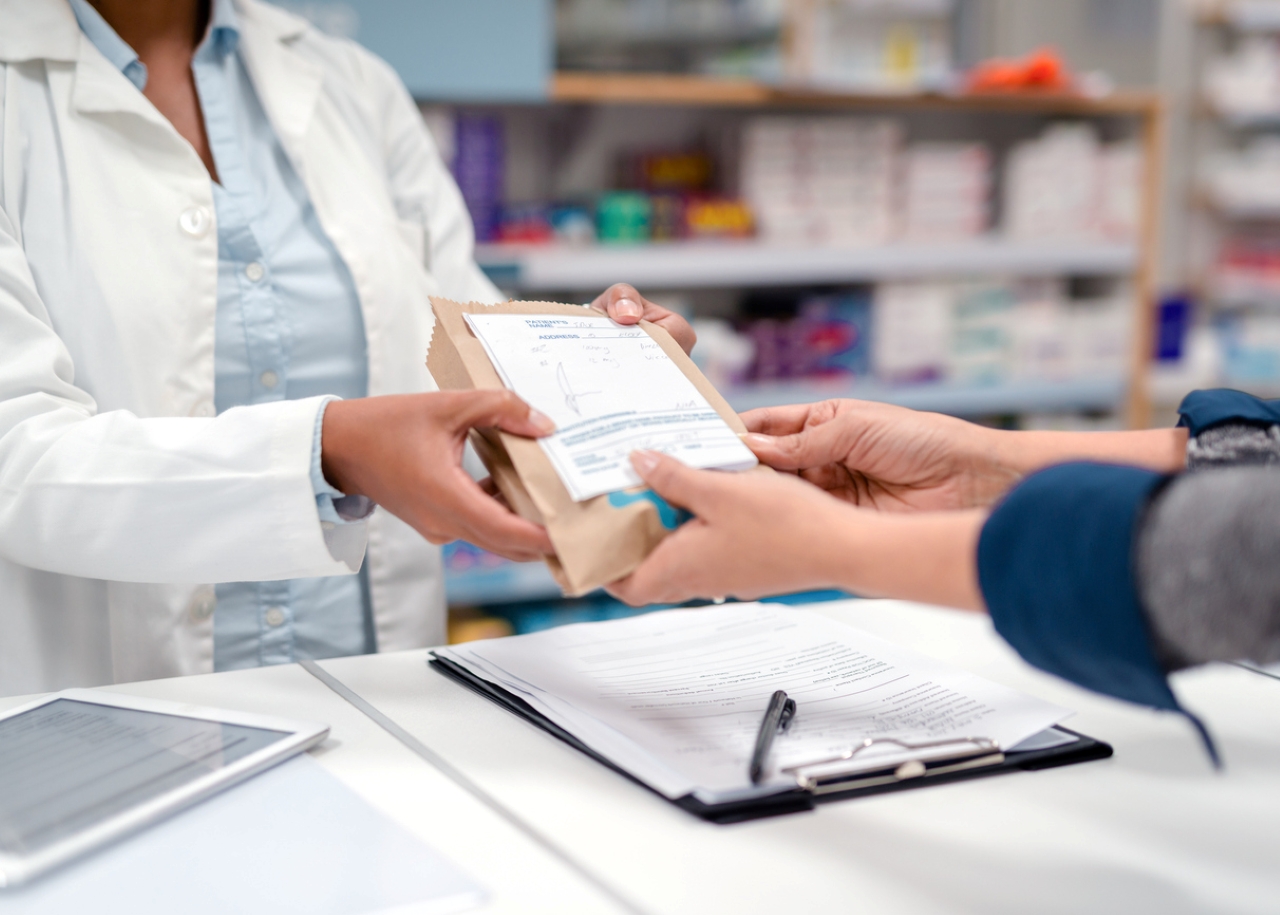 Pharmacist hands customer their prescription.