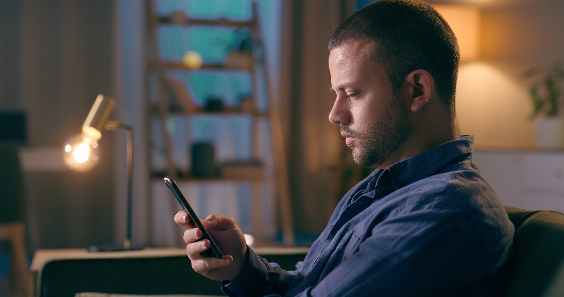 White male in room taring at mobile phone screen.