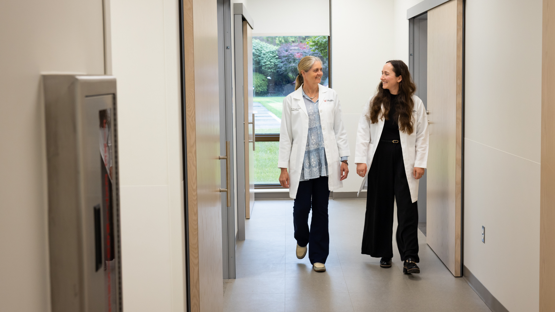 Two medical providers walk through a hallway. 