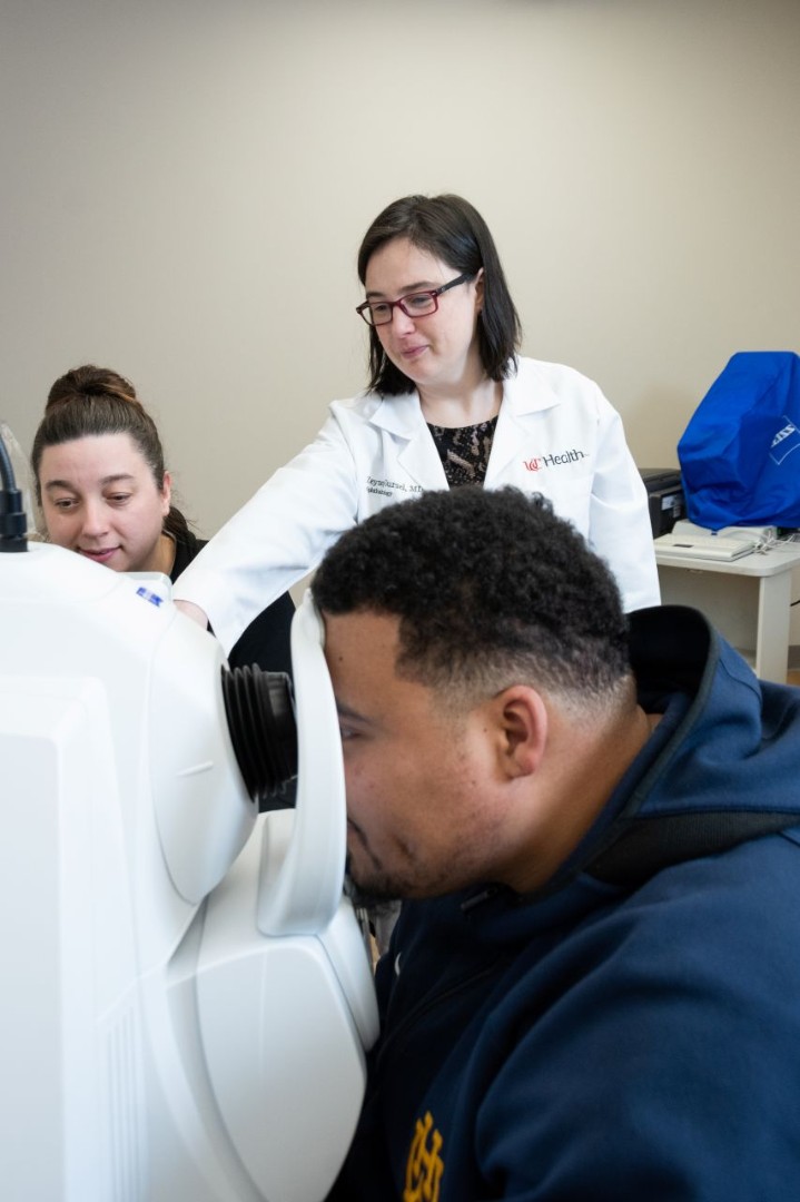 Physician watches as a patient looks through a medical device for eye treatment.