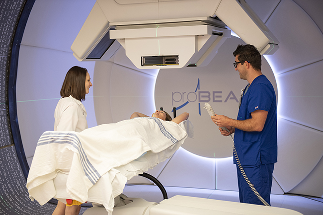 Medical providers talk with a patient receiving proton beam therapy.
