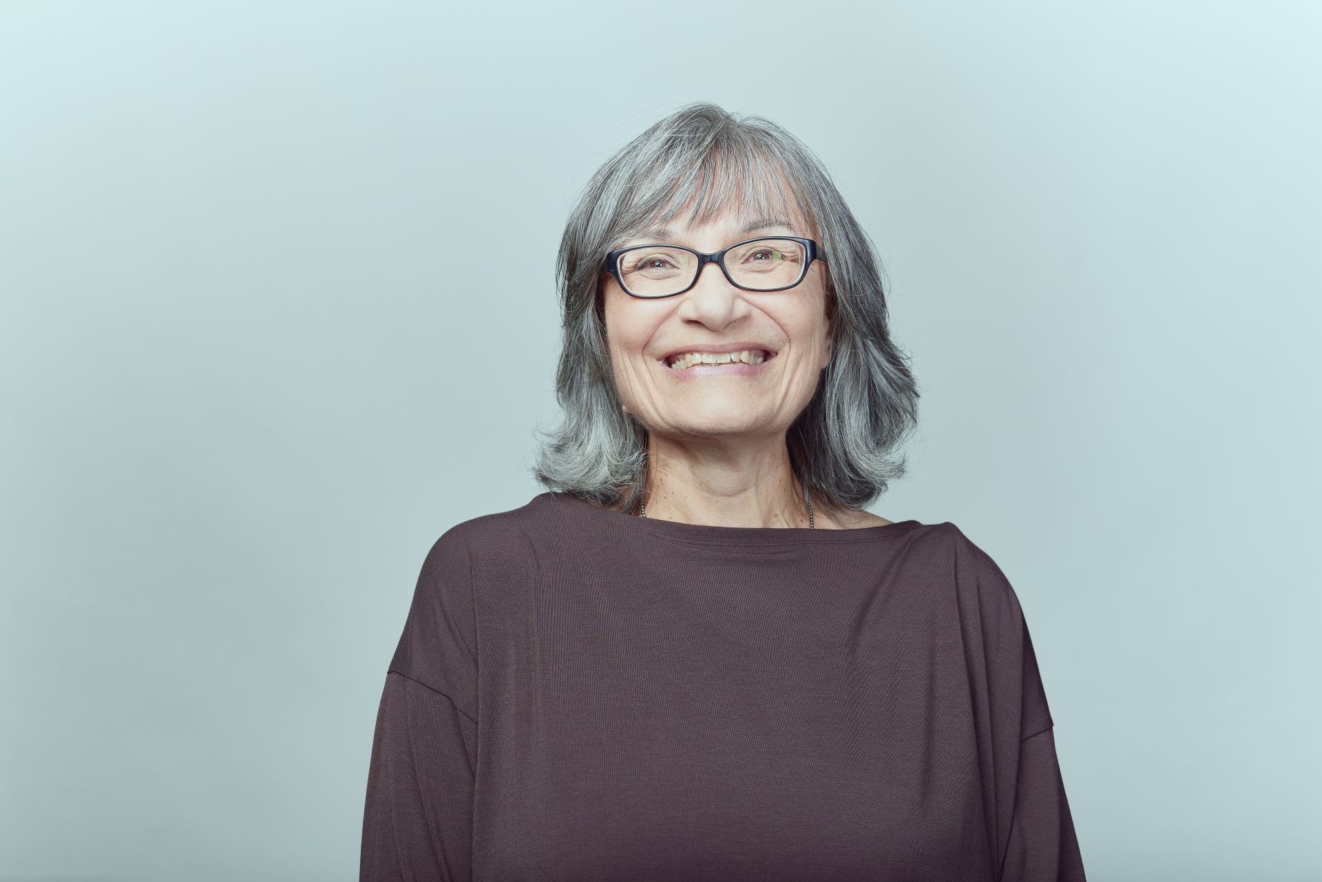 Maja smiling and standing in front of a grayish blue background. 
