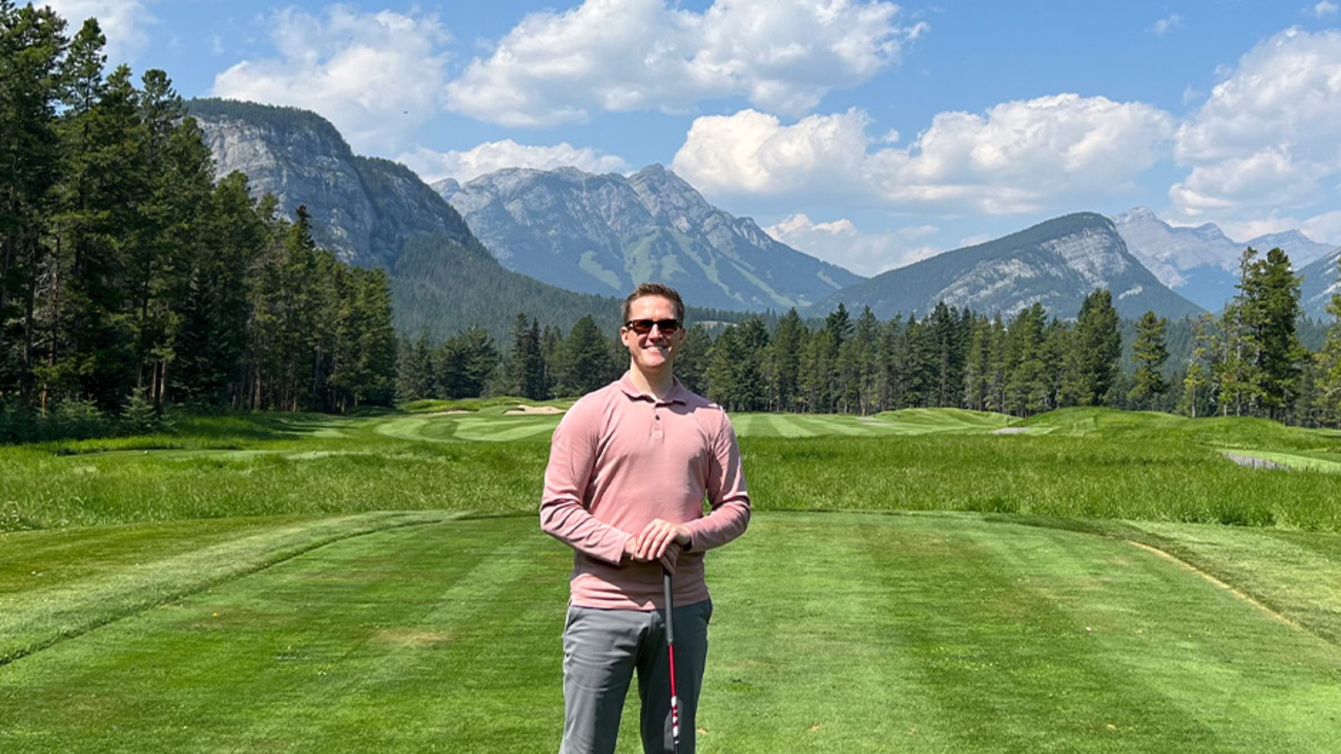 Kevin Mason poses with a golf club on a golf course in front of a mountain range