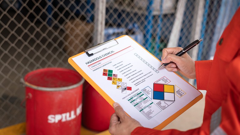 Safety officer checking chemical hazard material form for correct the oil spill kit which is placed at front of chemical storage warehouse area in factory.