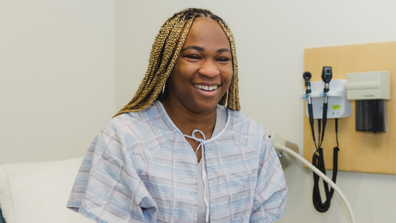Woman smiles while she sits on an examination table during an appointment at UC Heath in Cincinnati, Ohio