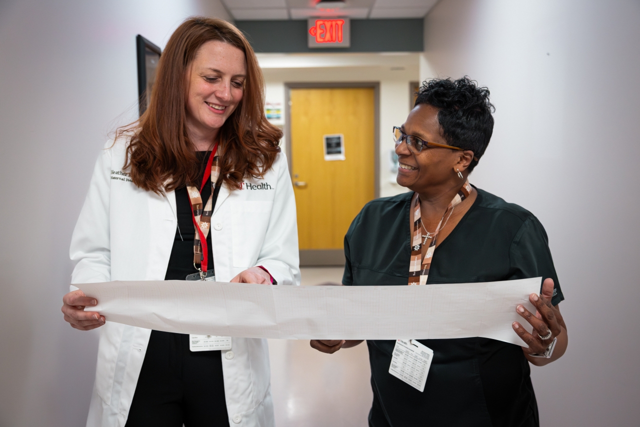 Physicians talk in a hallway while holding a document. 