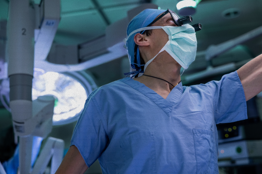 Surgeon is scrubs in operating room looks up at monitor.